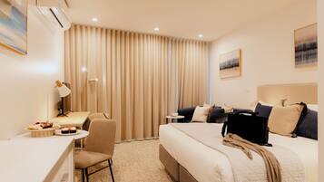 Habitación de hotel con cama, escritorio, silla, lámpara y ventana con cortinas.