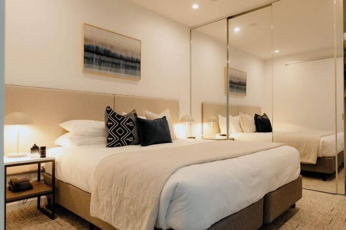 A hotel room with a large bed, bedside tables, a mirror, and a painting on the wall.