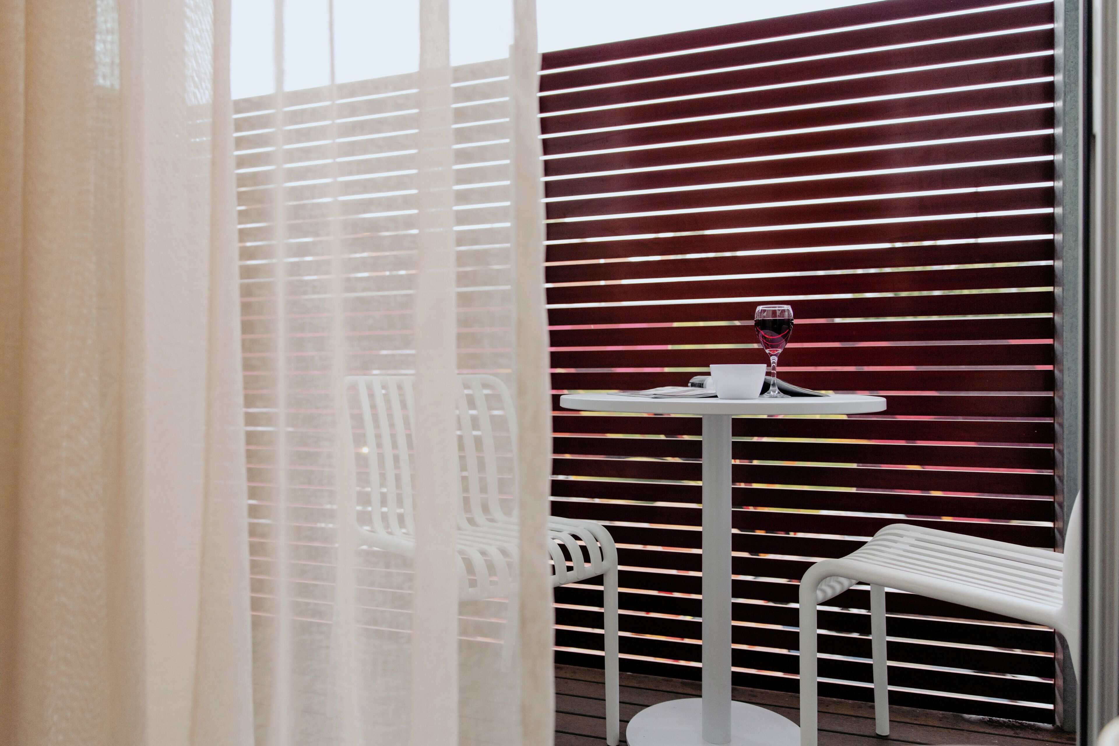A balcony with a table and chairs, a glass of red wine, and a wooden fence.