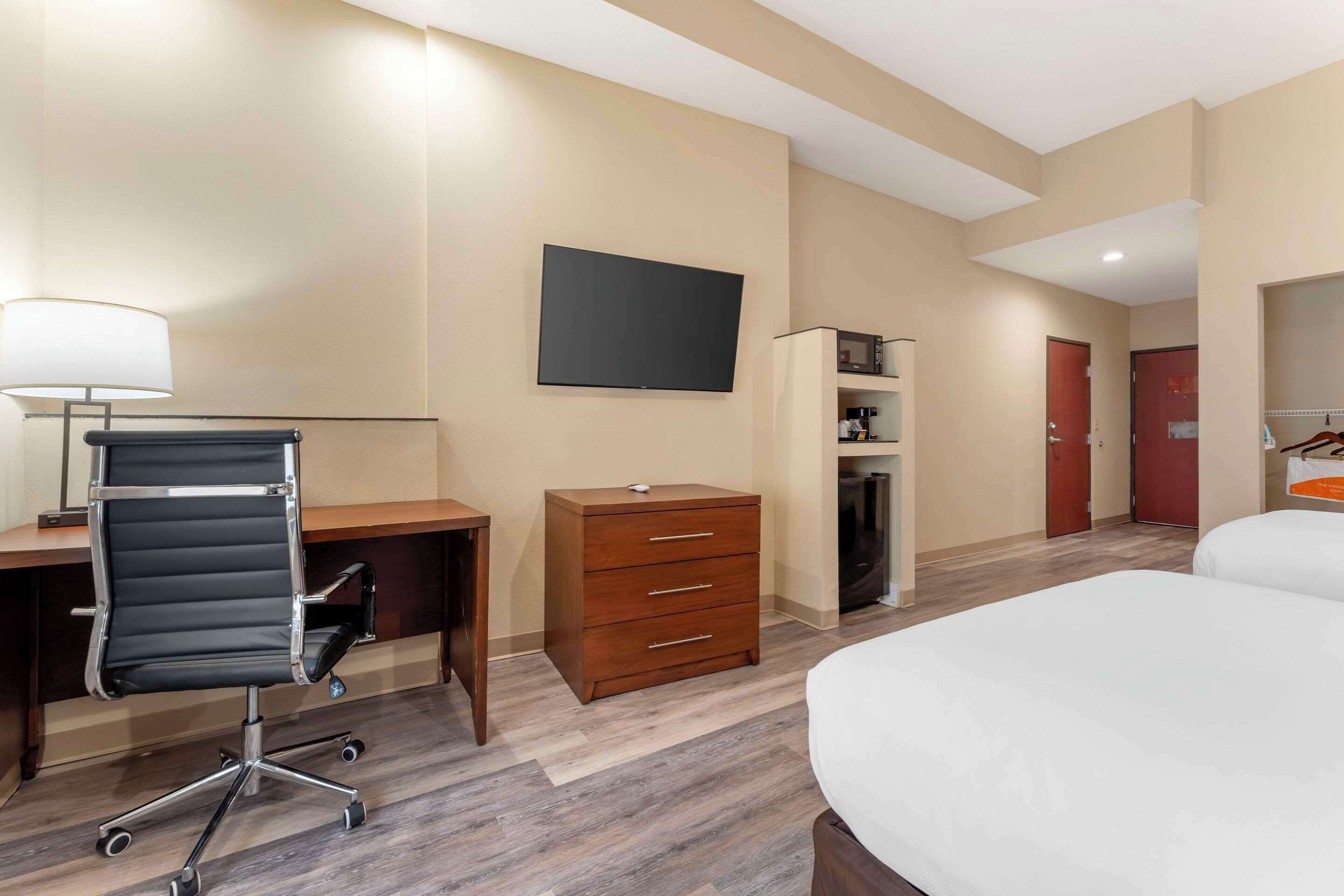 A hotel room with a desk, chair, dresser, TV, and two beds.