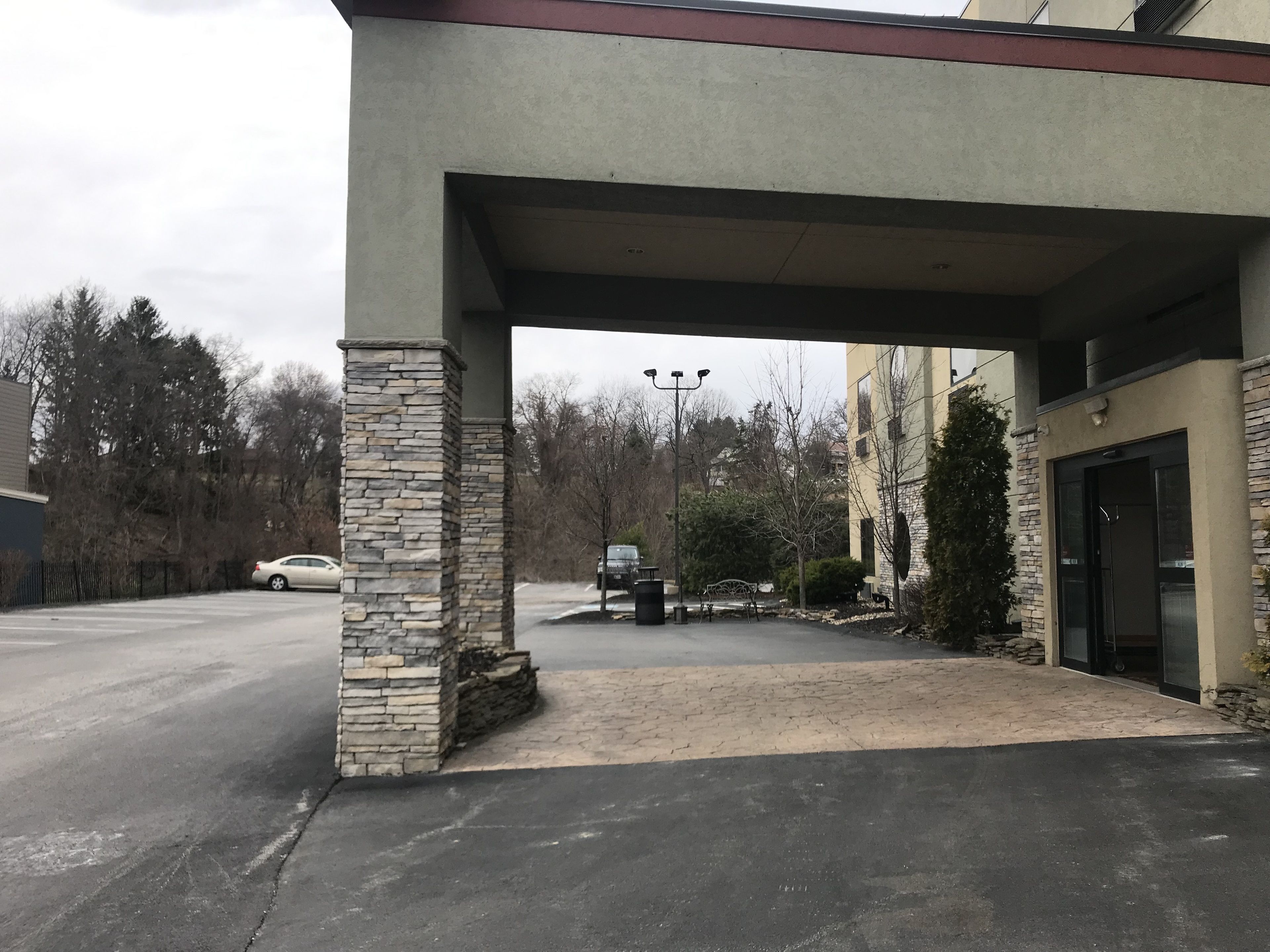 Una entrada cubierta con pilares de piedra, un camino de entrada pavimentado y un coche estacionado.