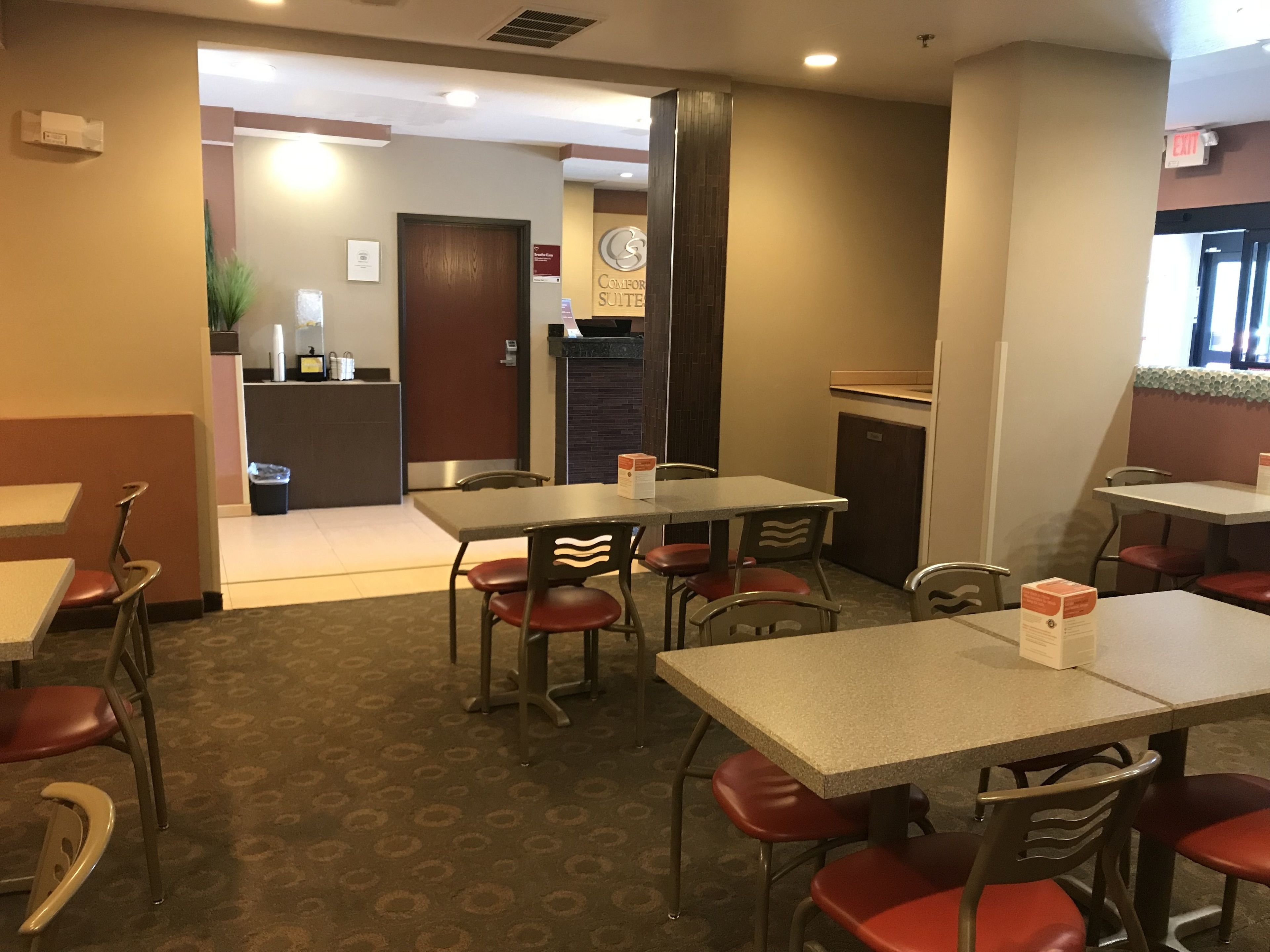 Un hall d’hôtel avec plusieurs tables et chaises, un comptoir de réception et un panneau indiquant clairement la sortie.