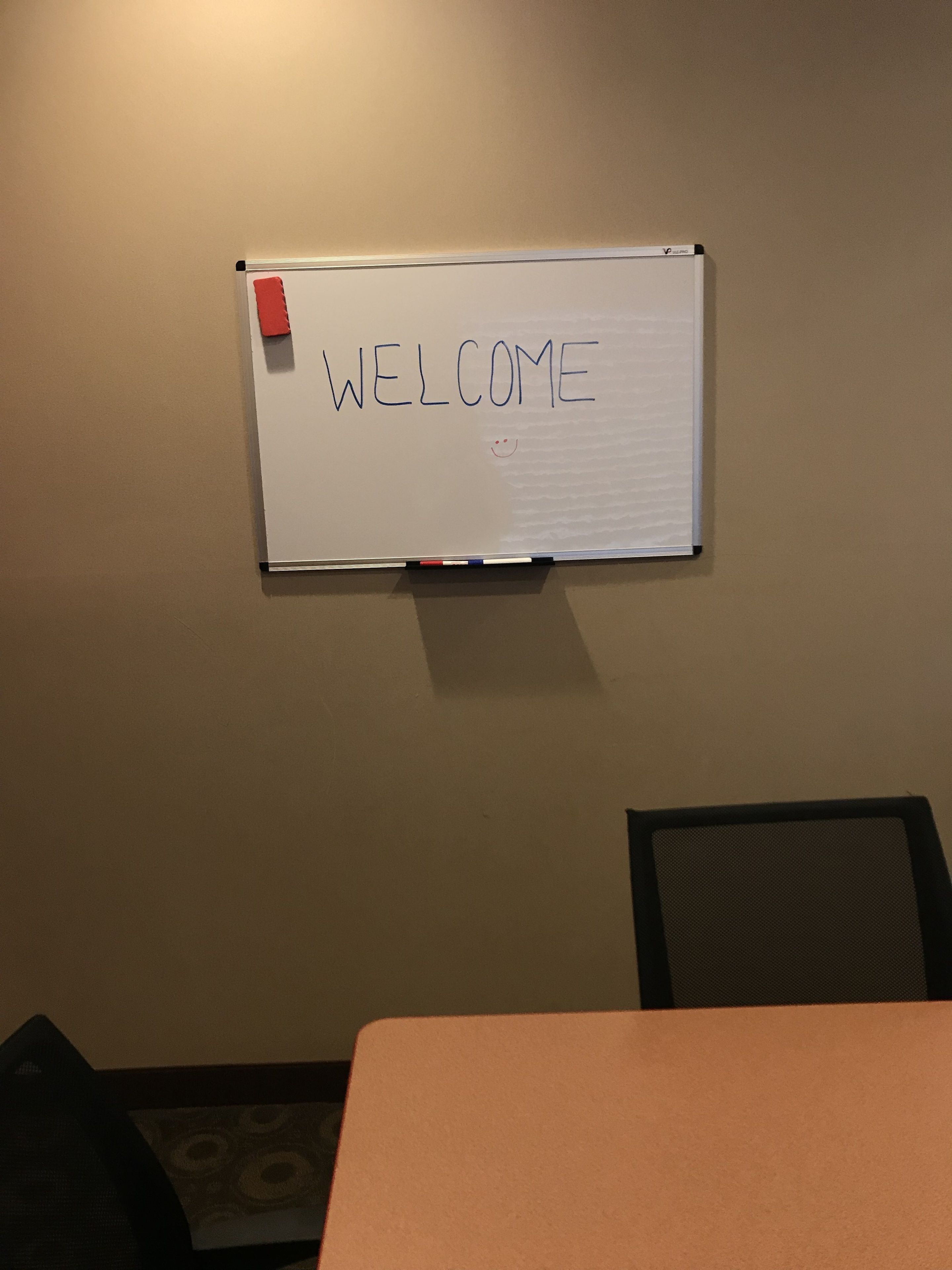 Een whiteboard waarop 'WELCOME' staat, een rode plakbriefje en een gaaswand.