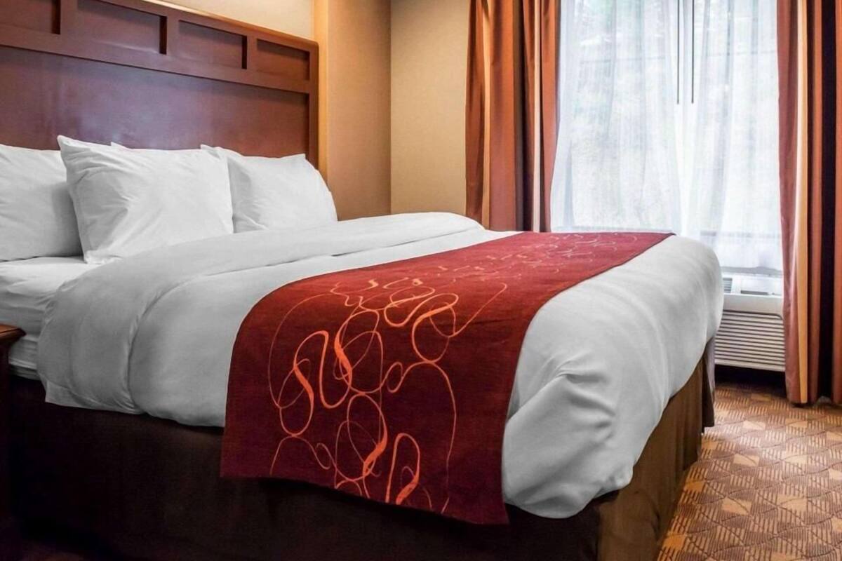 Ett hotellrum med en säng, en sänggavel i trä, ett fönster med gardiner och ett golv täckt av matta.