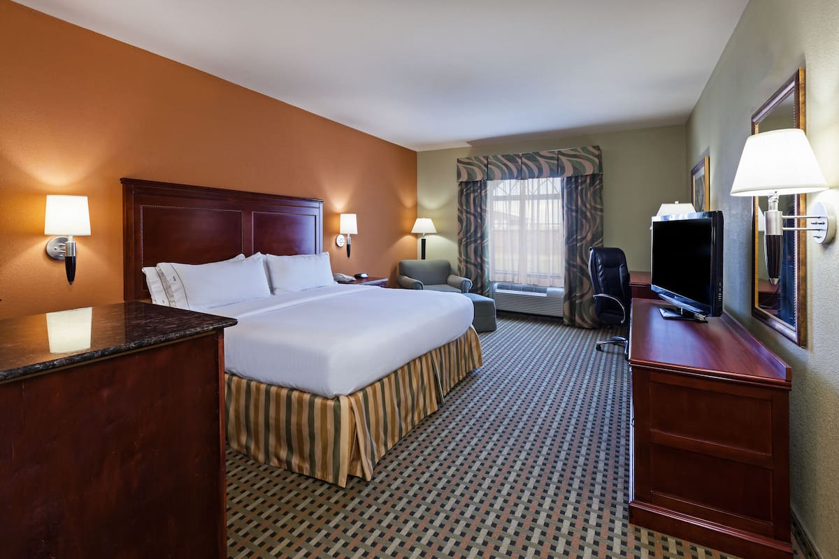 A hotel room with a large bed, a desk, a chair, a television, and a window with curtains.