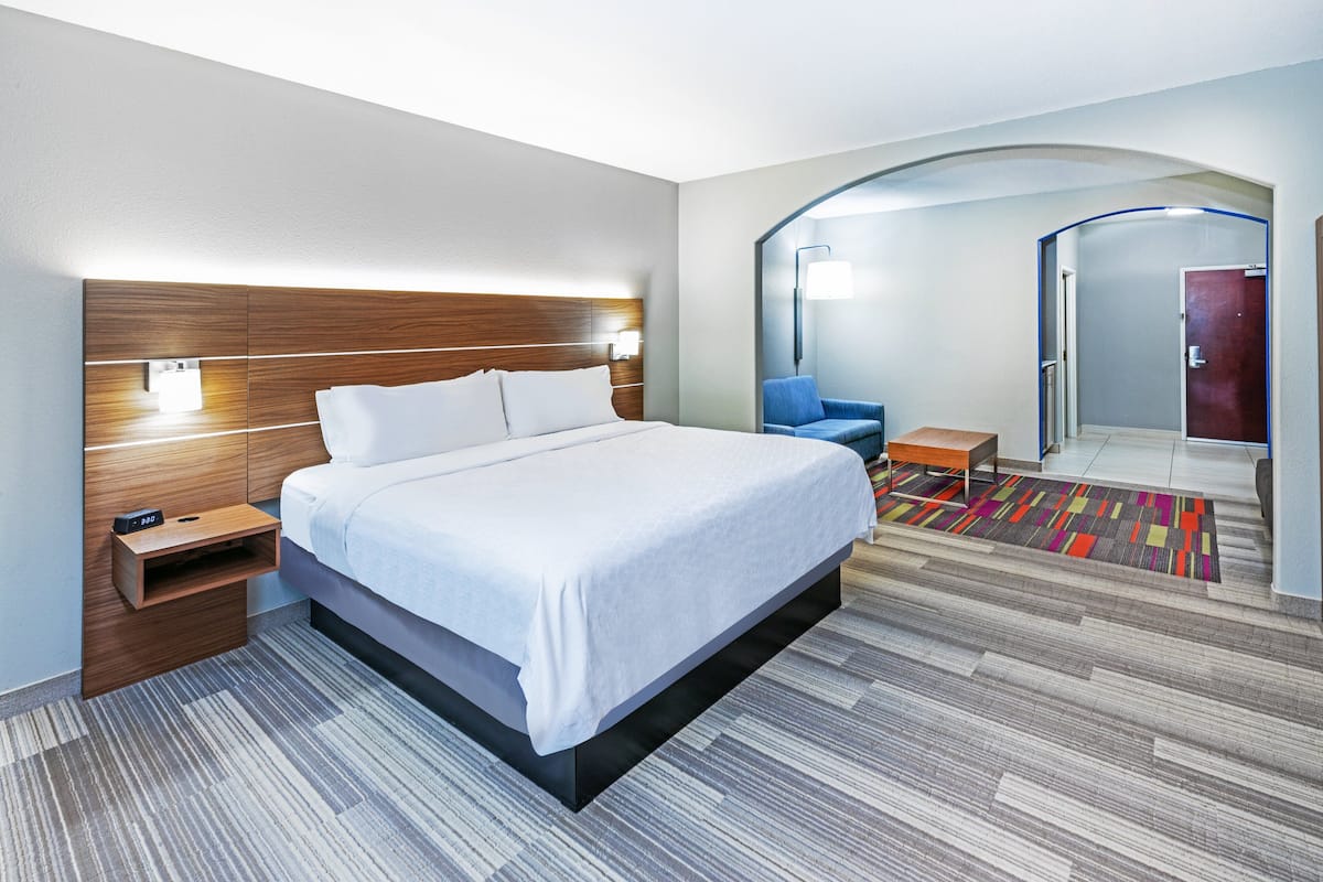 A modern hotel room with a large bed, a nightstand, a chair, and a mirror.