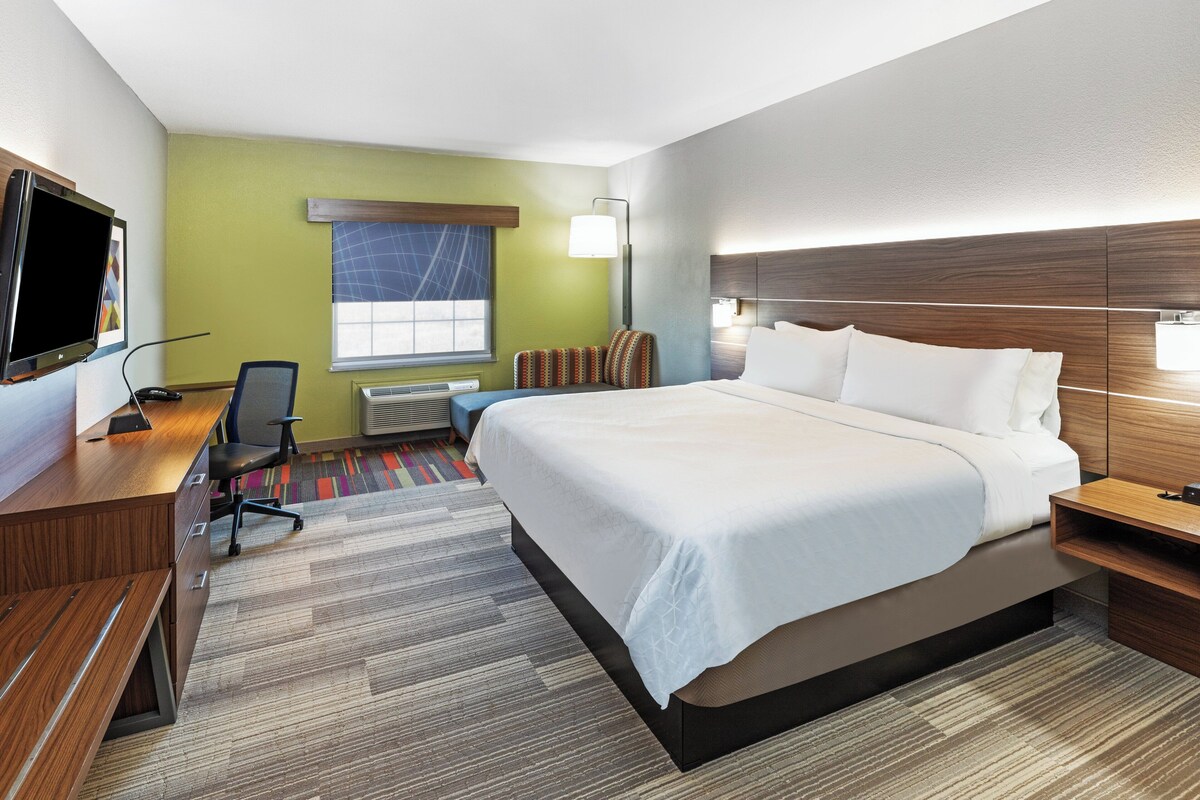 Een hotelkamer met een groot bed, een bureau met stoel, een flatscreen-tv en een raam met luxaflex.