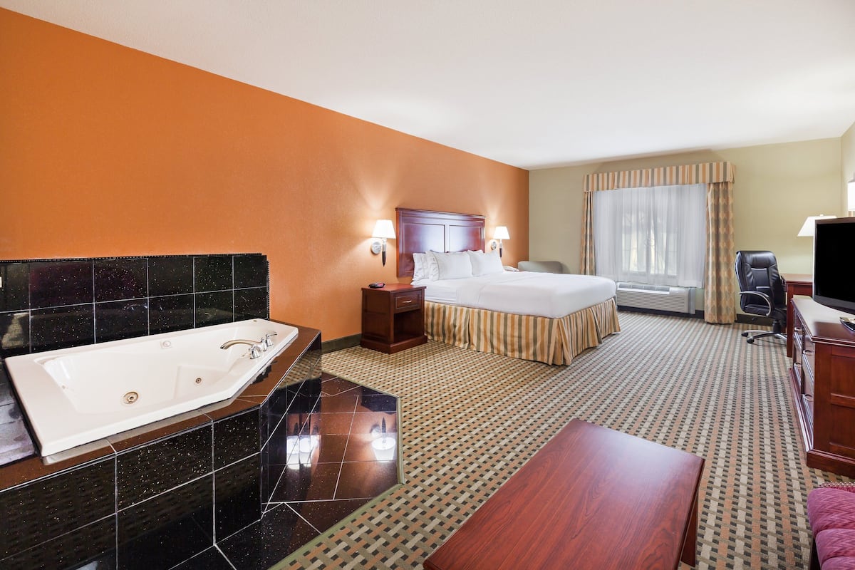 A hotel room with a large bathtub, a bed with a wooden headboard, a desk, and a television.