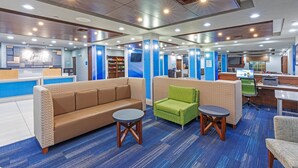 A modern hotel lobby with a blue carpet, a brown sofa, a green armchair, and a small round table. - Holiday Inn Express & Suites East Amarillo by IHG (Amarillo)