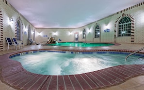 An indoor swimming pool with a brick wall and arched windows, surrounded by lounge chairs and a tiled deck. - Holiday Inn Express & Suites East Amarillo by IHG (Amarillo)