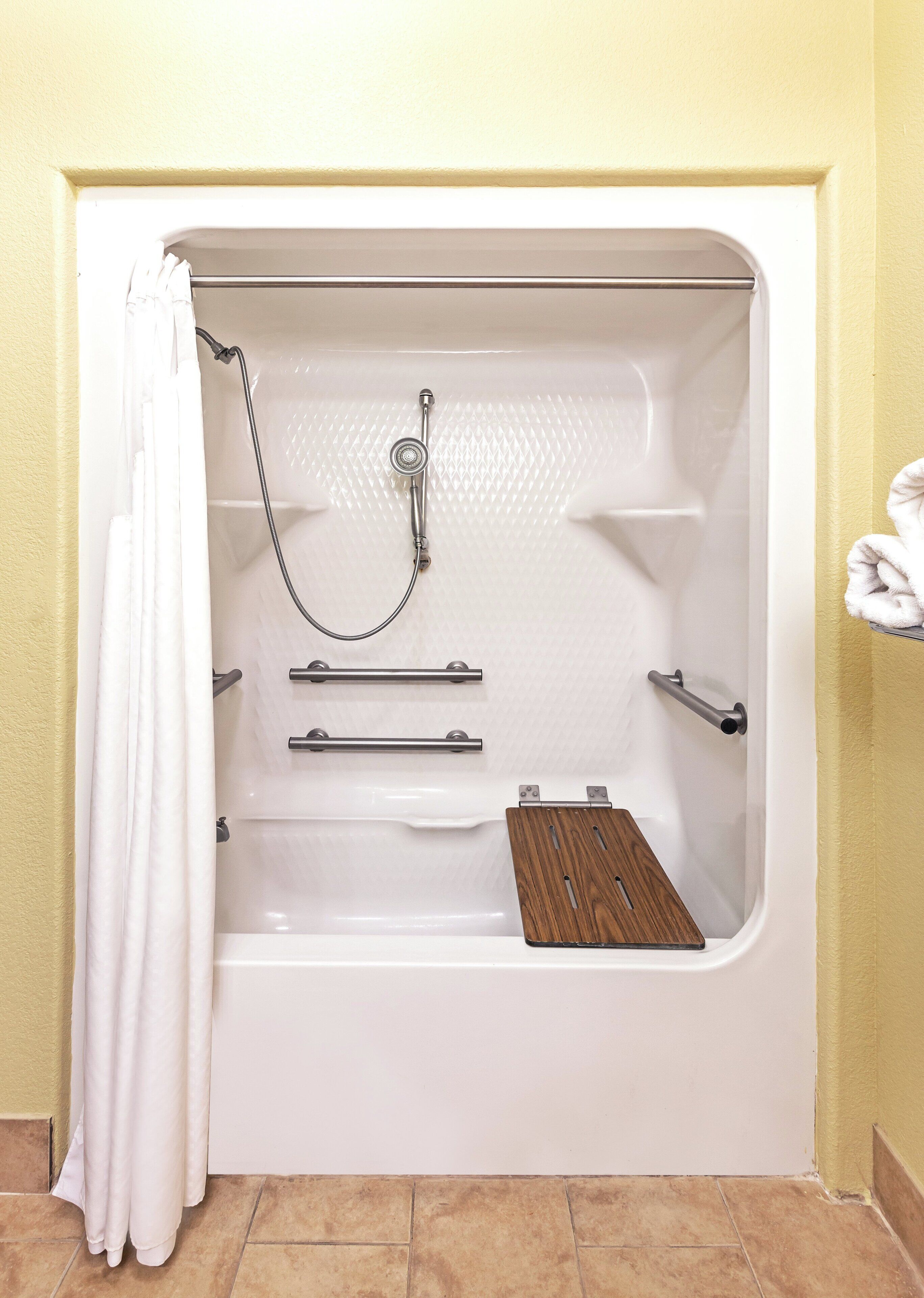 A bathtub with a showerhead, grab bars, and a wooden shelf.