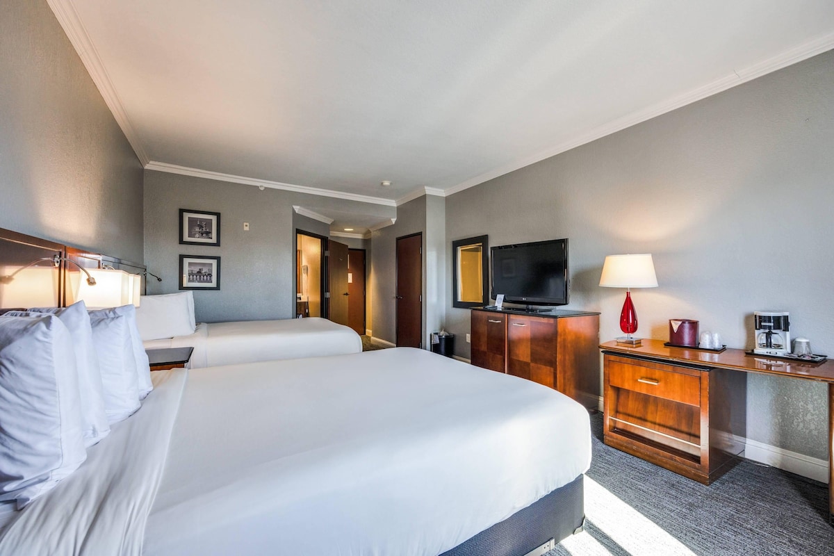 A hotel room with a large bed, a desk with a television, a lamp, and a coffee maker.