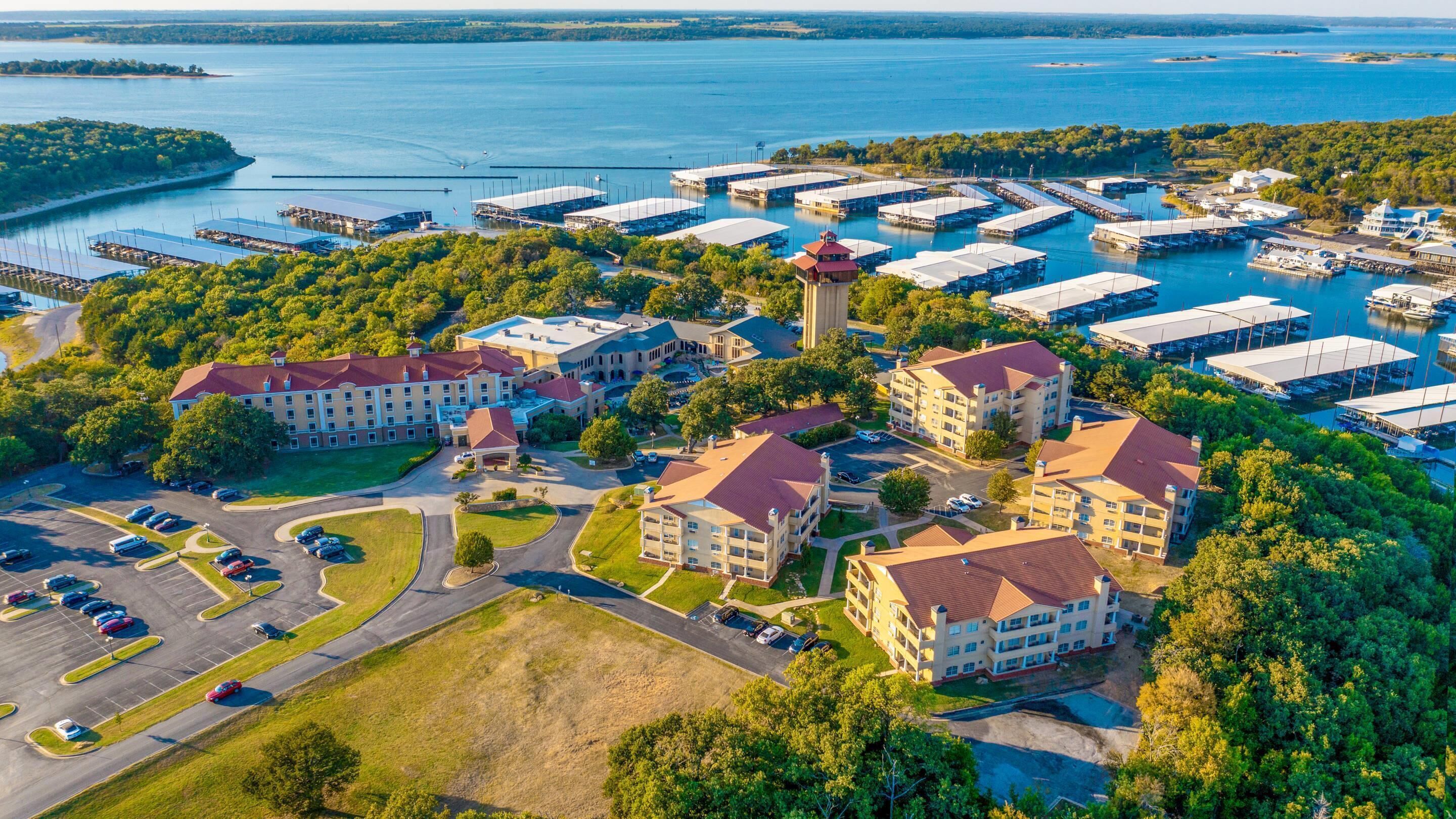 A marina with multiple docks and boats, surrounded by lush greenery and a large hotel with multiple buildings.