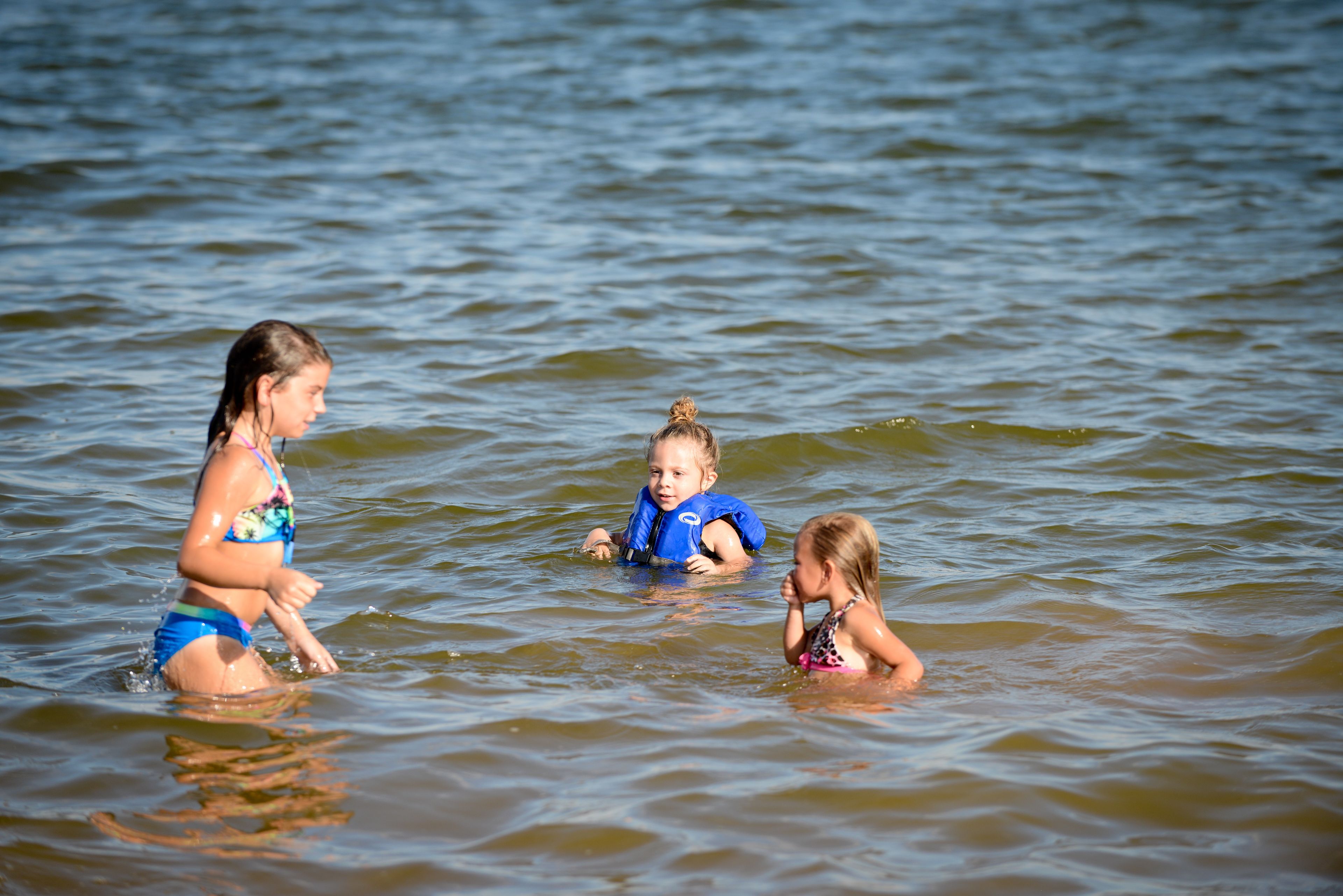 Three people in a body of water, wearing life jackets.