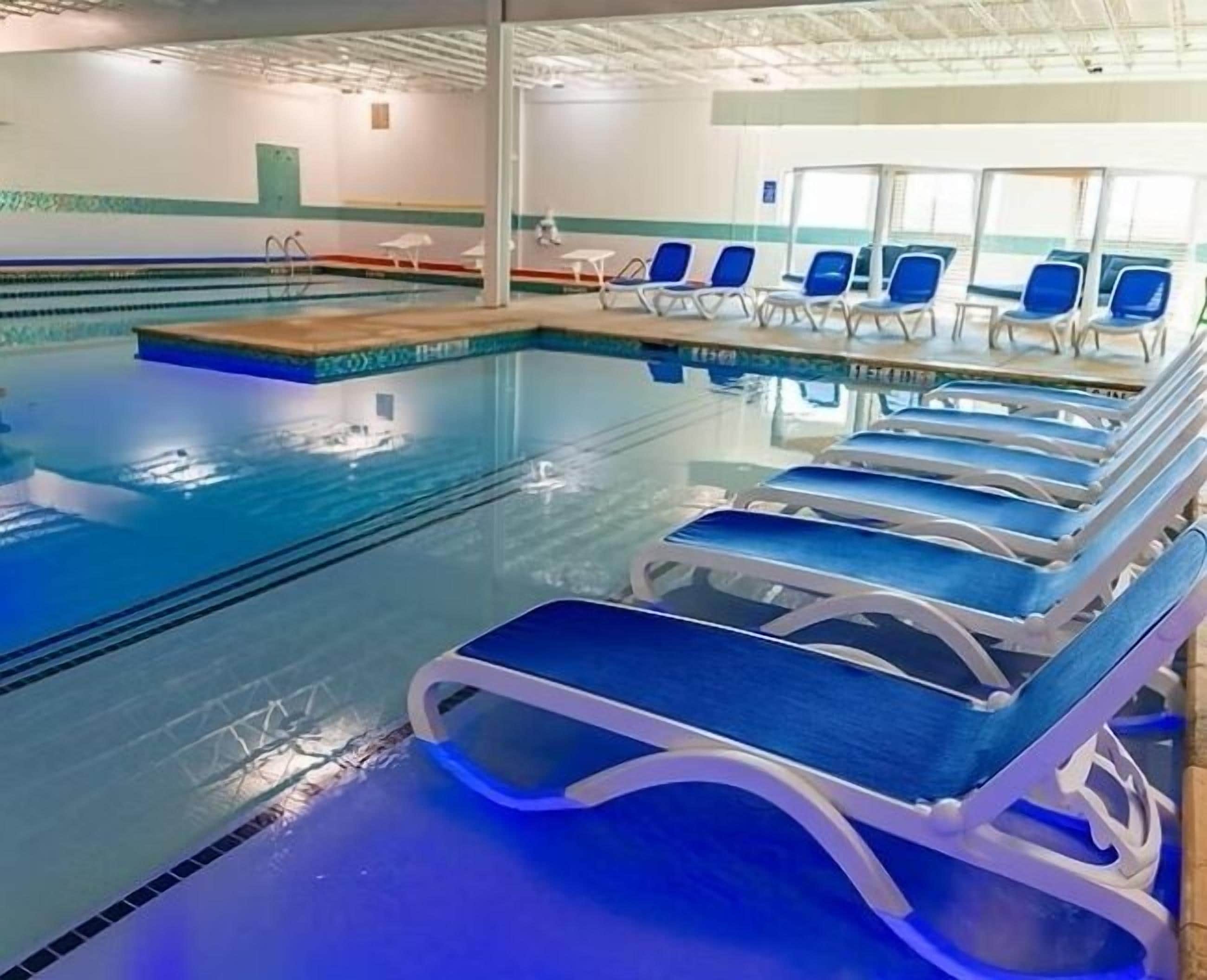 An indoor swimming pool with blue lounge chairs and a tiled deck area.