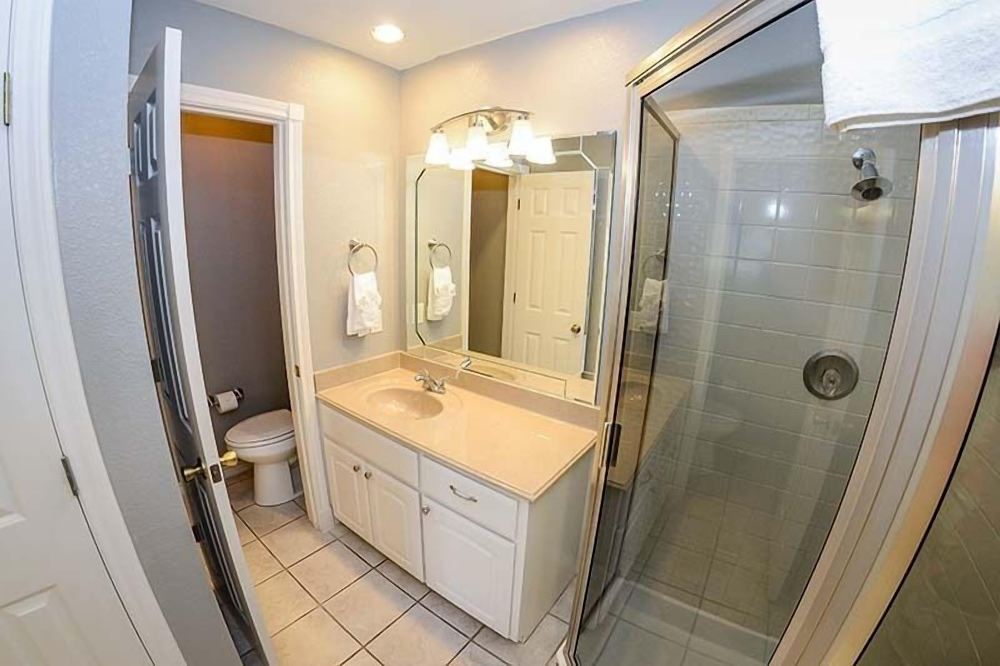 Un baño con lavamanos, espejo, inodoro y cabina de ducha de vidrio.