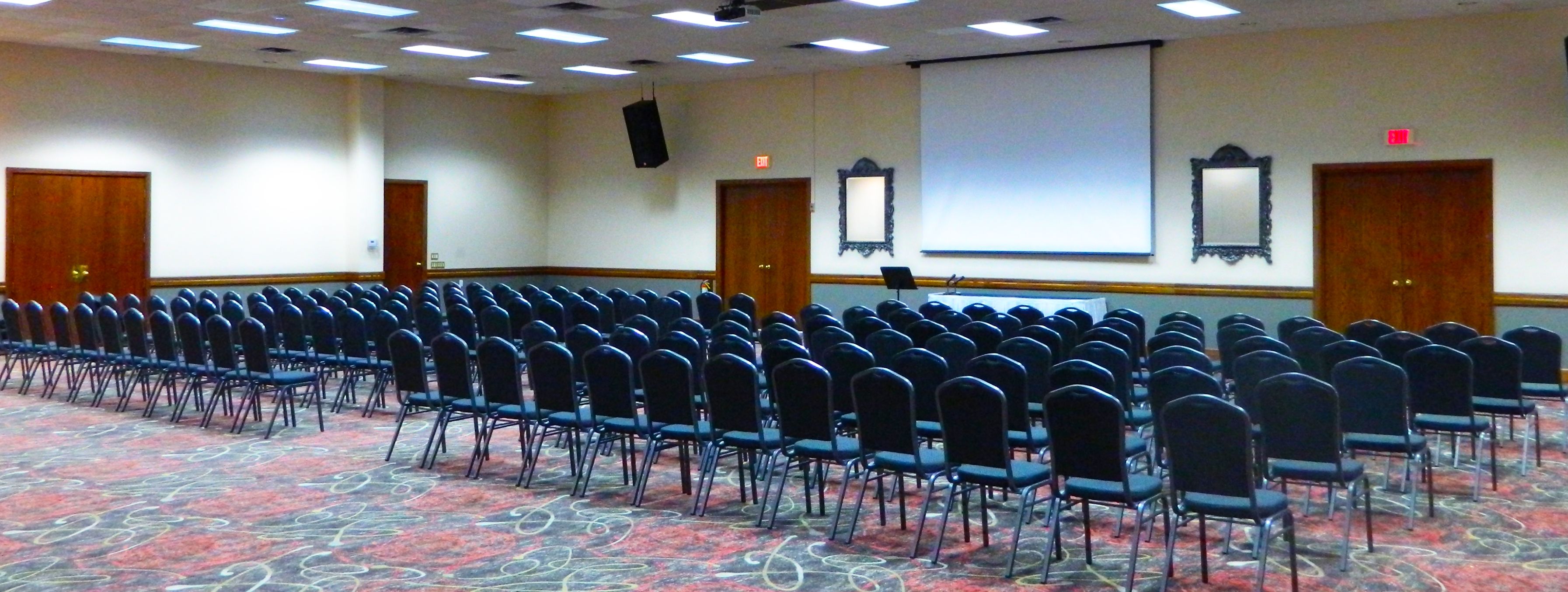 A conference room with rows of chairs, a projector screen, and a carpeted floor.