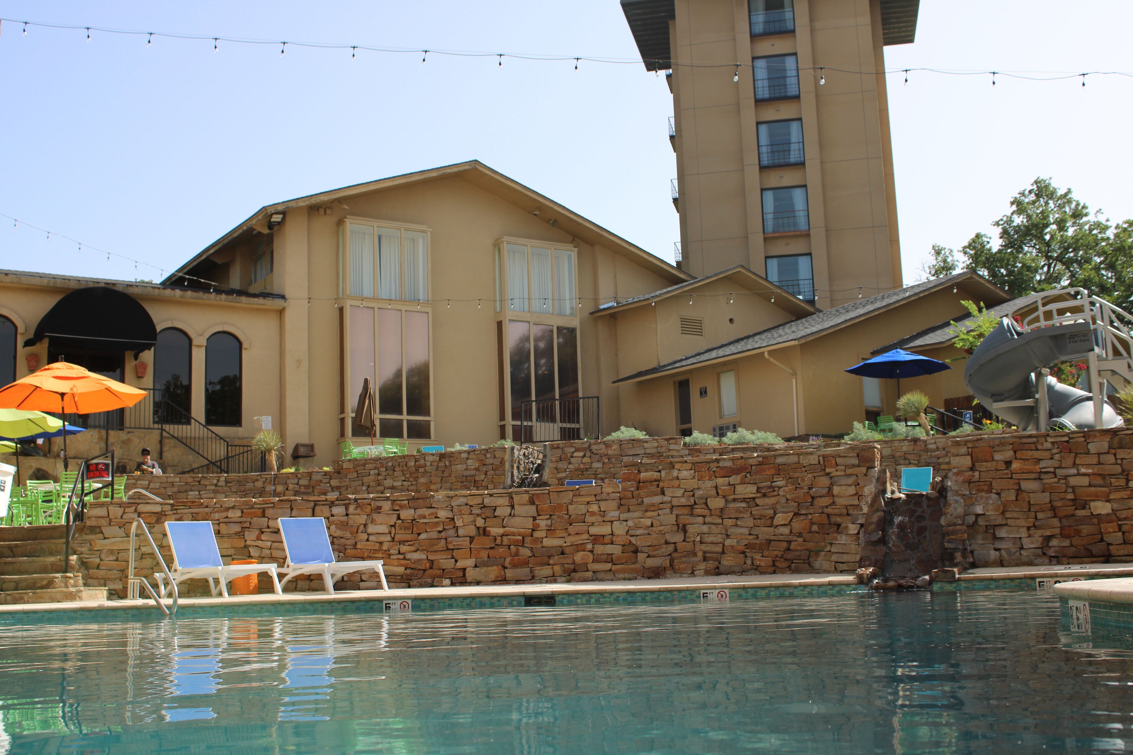 A hotel with a pool area, stone wall, and a large building with multiple windows and balconies.