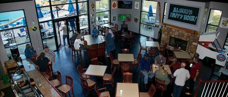 Un restaurant doté de nombreuses tables et chaises, d’une cheminée en pierre et de grandes fenêtres donnant sur l’extérieur.
