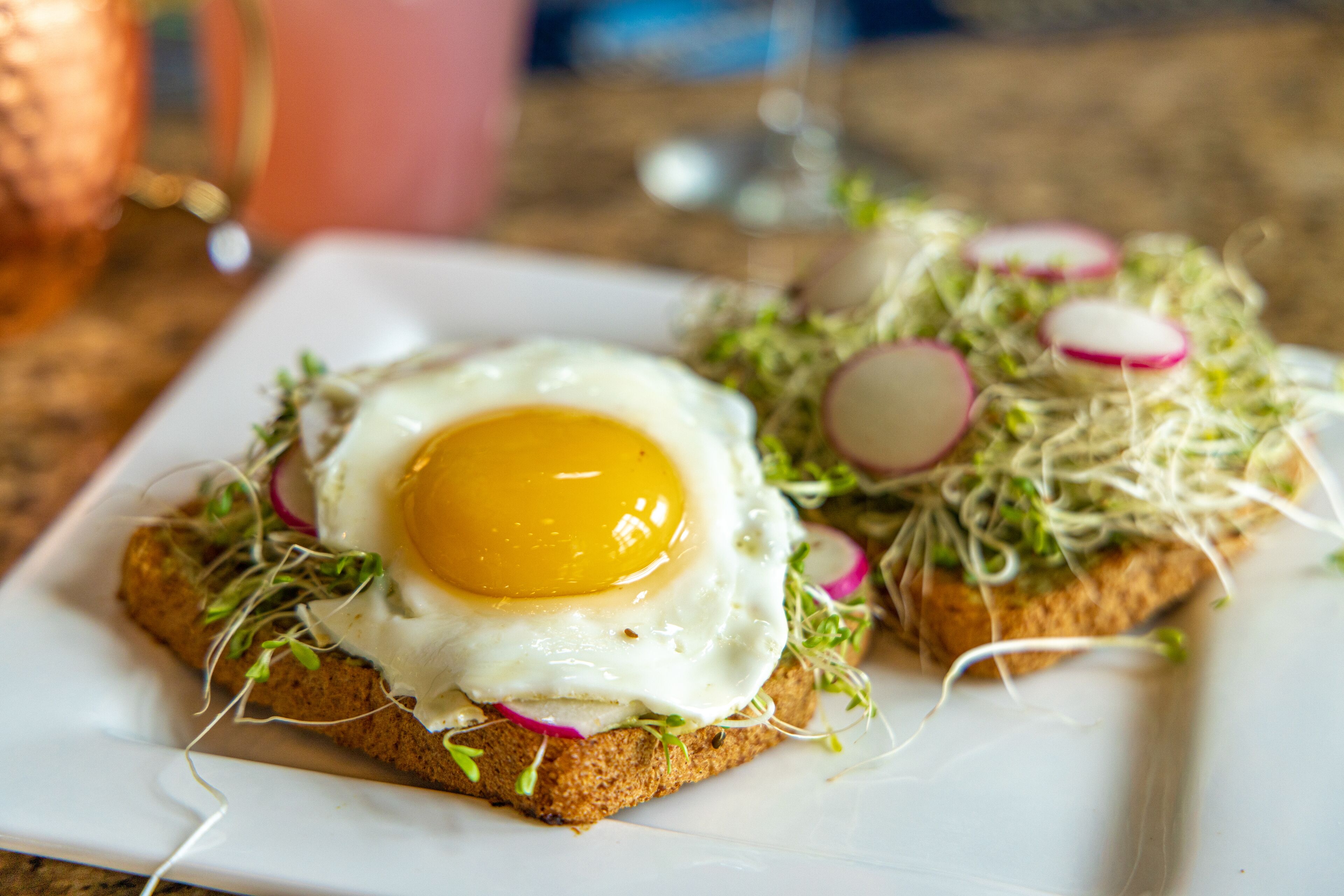 A plate with a fried egg on a slice of bread topped with sprouts and radish slices.