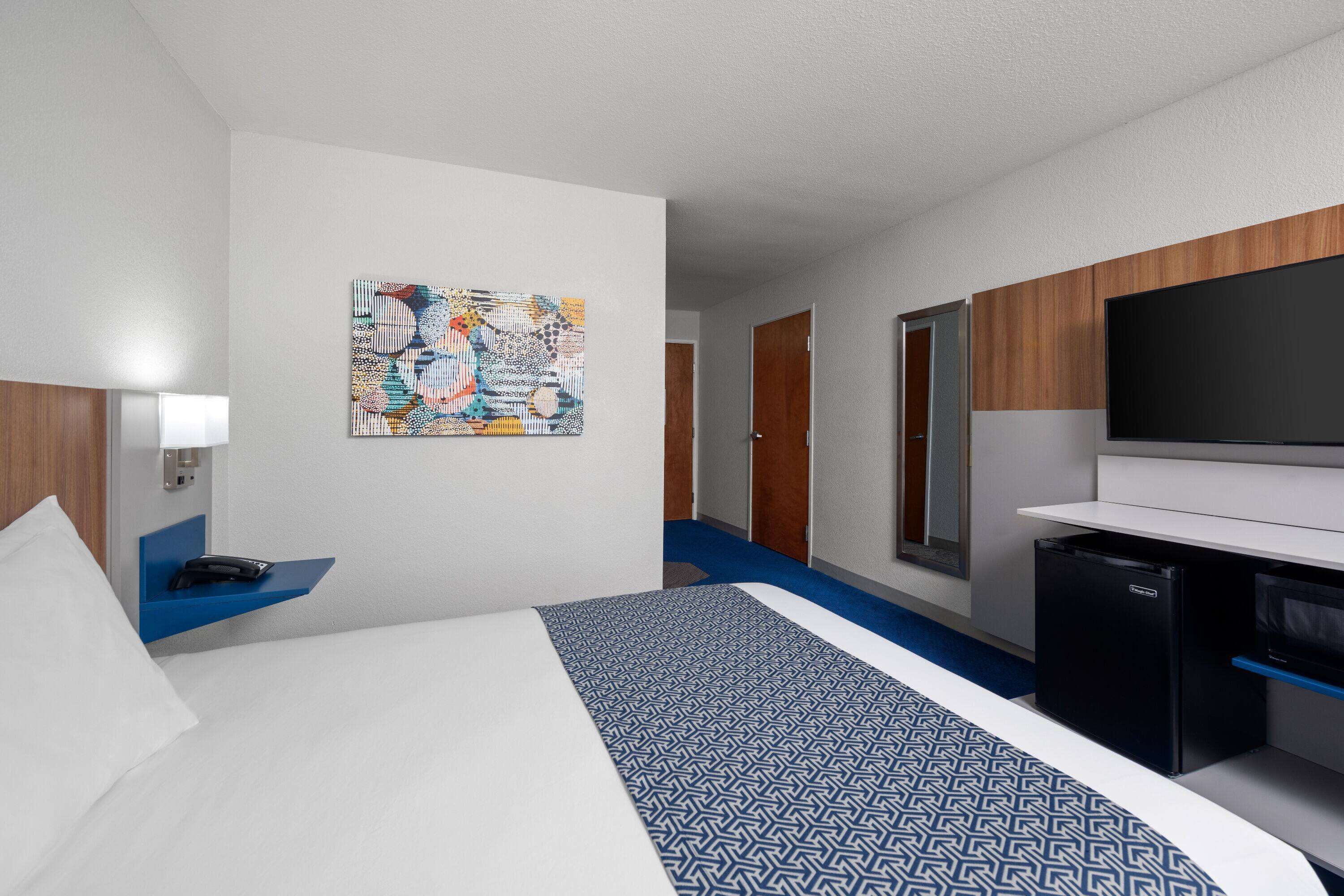 Una habitación de hotel con cama, escritorio, televisión y un refrigerador pequeño.
