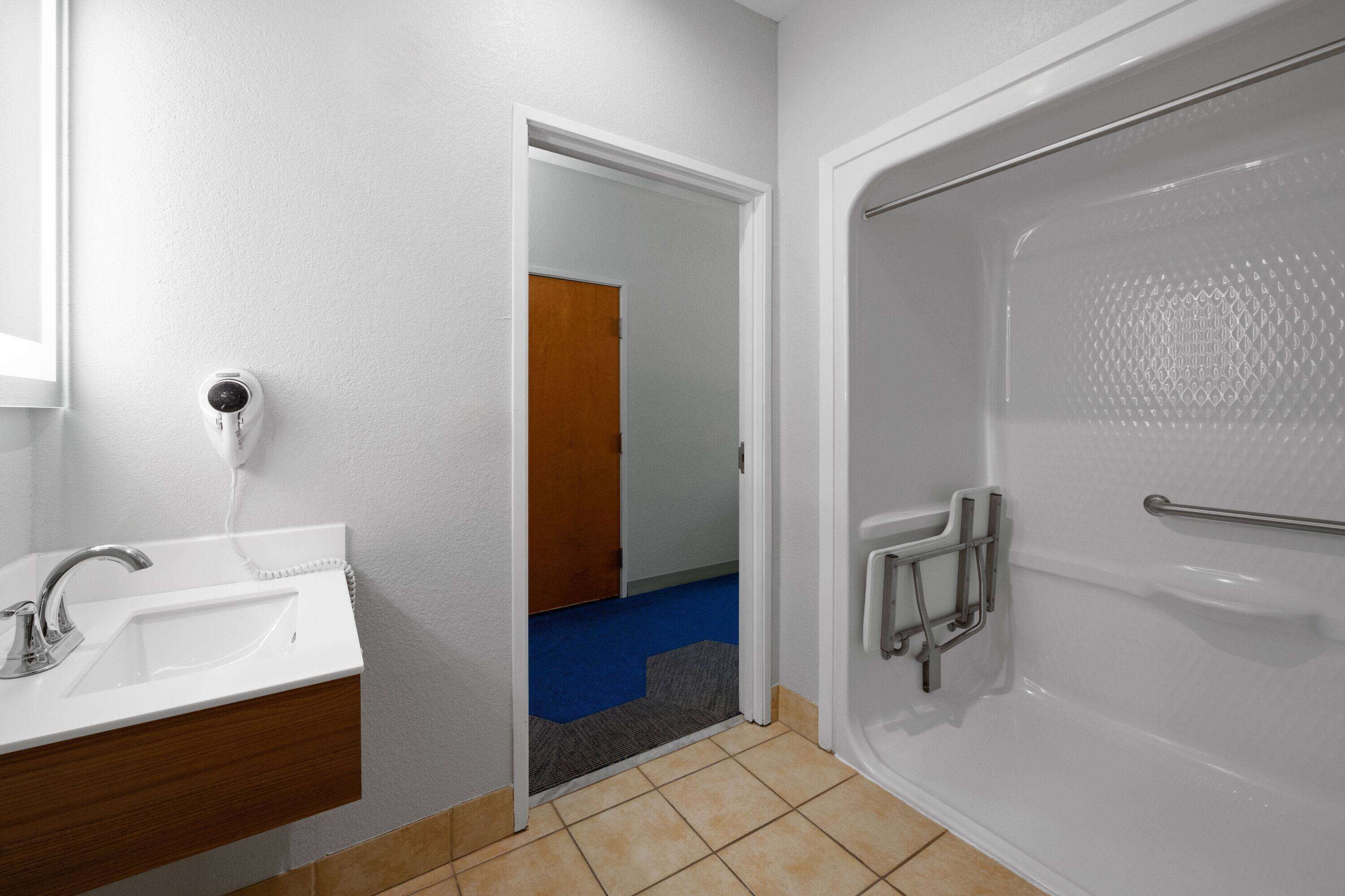 A bathroom with a white sink, a shower with a grab bar, and a door leading to another room.