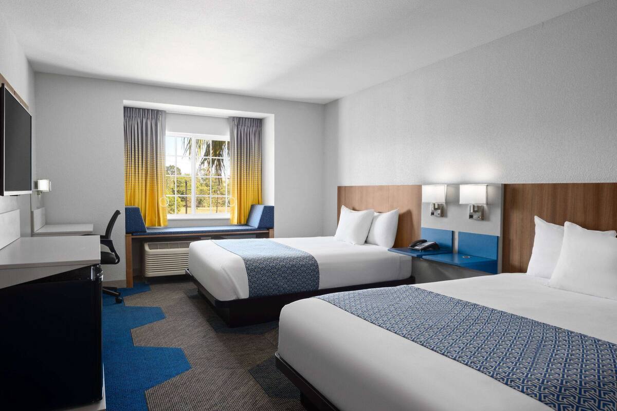 A hotel room with two beds, a desk, a chair, a TV, and a window with curtains.