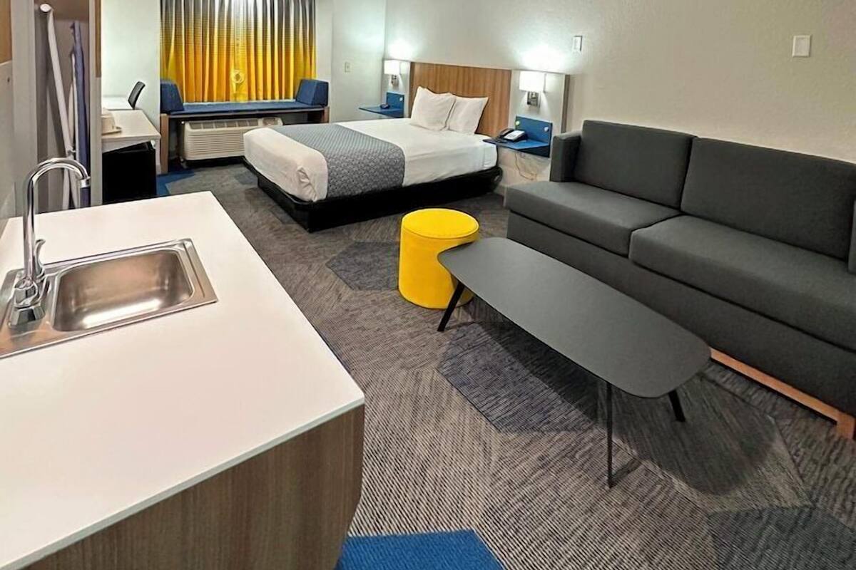 A hotel room with a bed, a sofa, a desk with a chair, a sink, and a window with curtains.