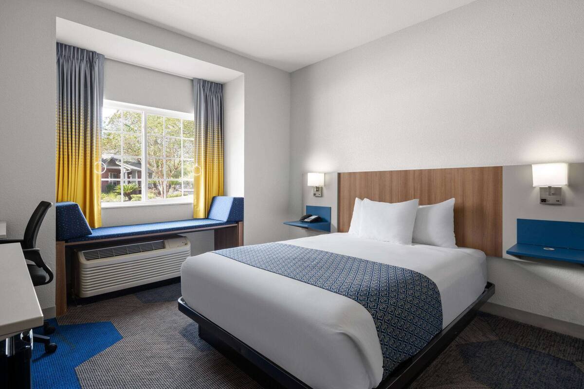 A hotel room with a large bed, a desk, a chair, and a window with curtains.