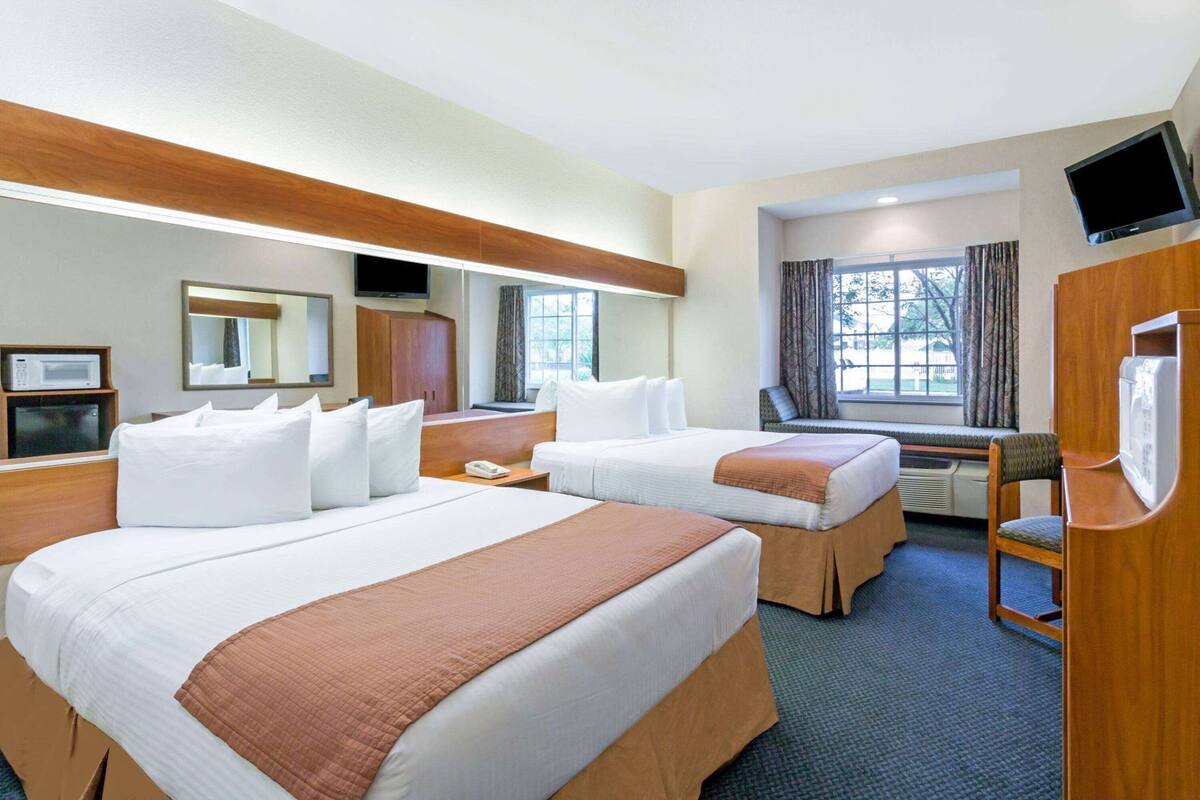 A hotel room with two beds, a TV, a microwave, a desk, and a window with curtains.