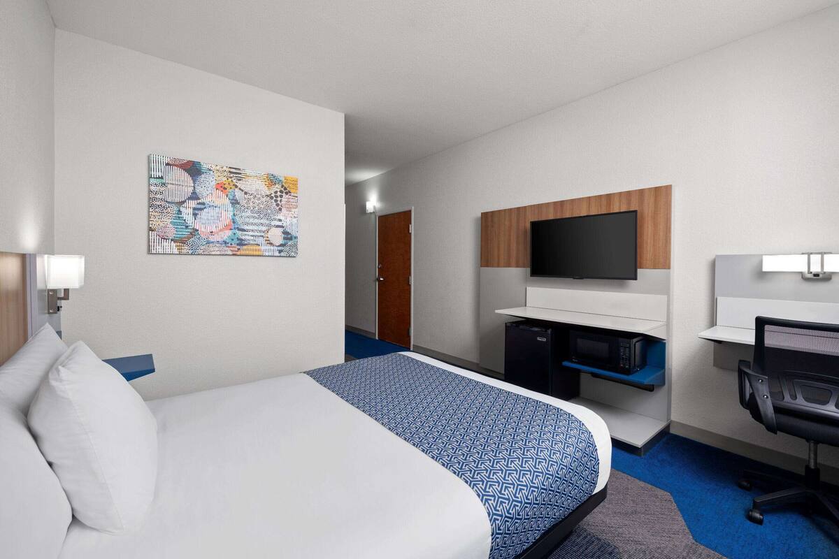 A hotel room with a bed, a desk, a television, and a microwave.