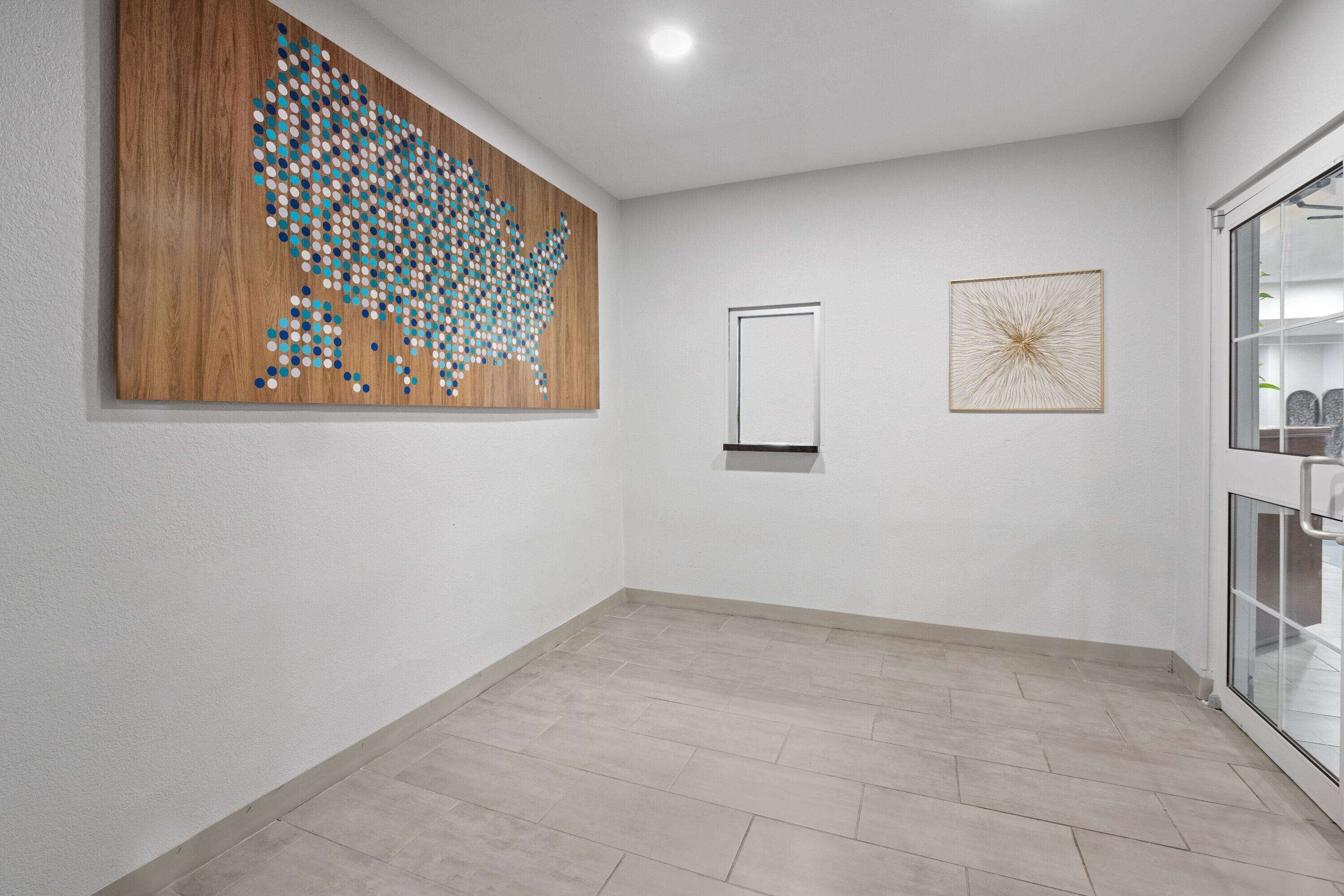 A spacious room with a large wooden wall art piece, a framed abstract artwork, and a glass-fronted storage unit.