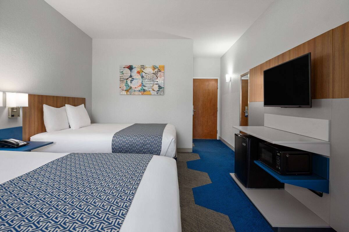A hotel room with two beds, a flat-screen TV, a microwave, and a small kitchenette.