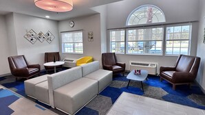 Un área de descanso moderna con un sofá modular, sillones de cuero, una mesita y un reloj decorativo en la pared.