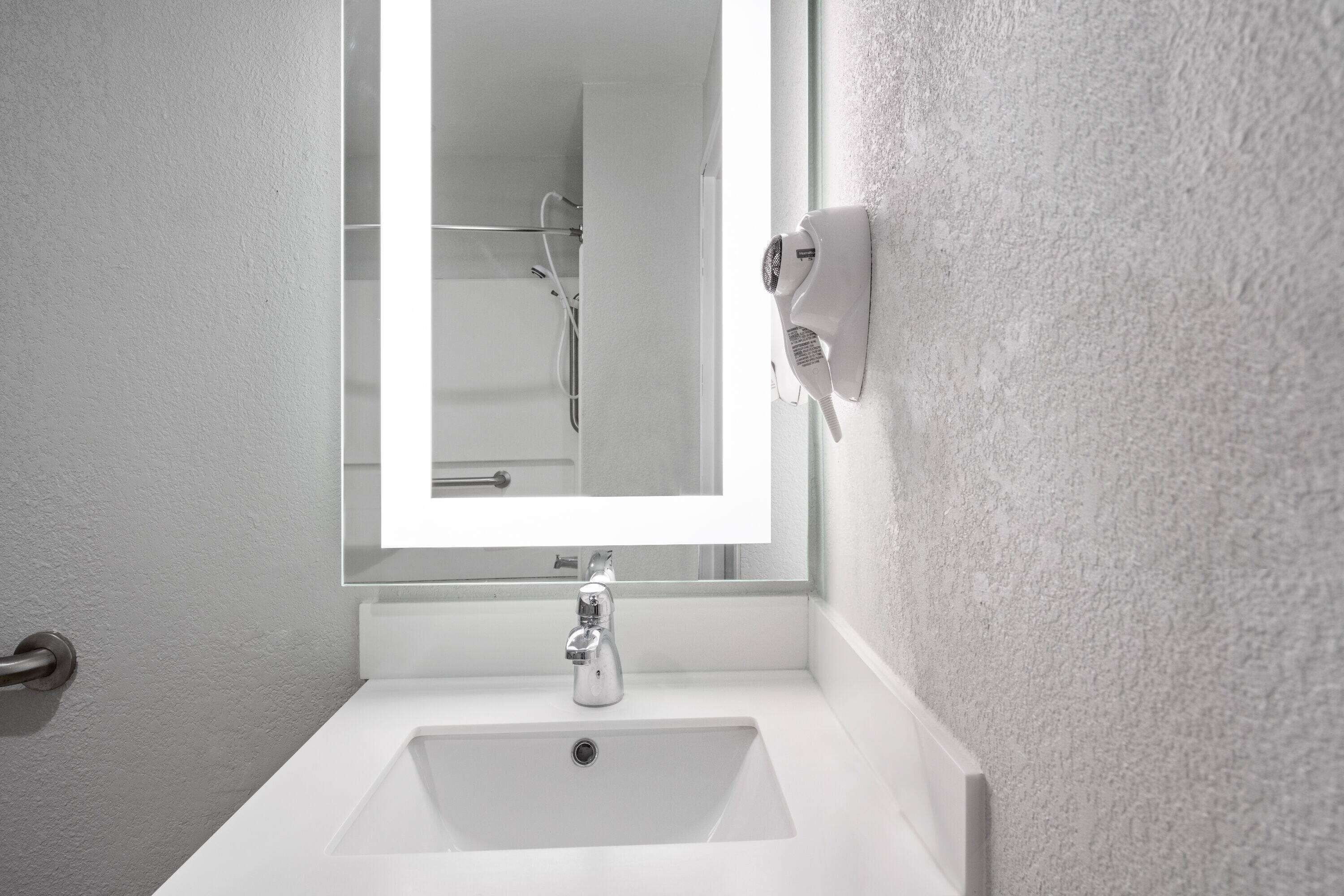 A bathroom with a white sink, a mirror, and a handheld showerhead.