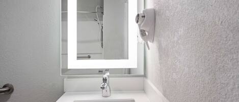 A bathroom with a white sink, a mirror, and a handheld showerhead.