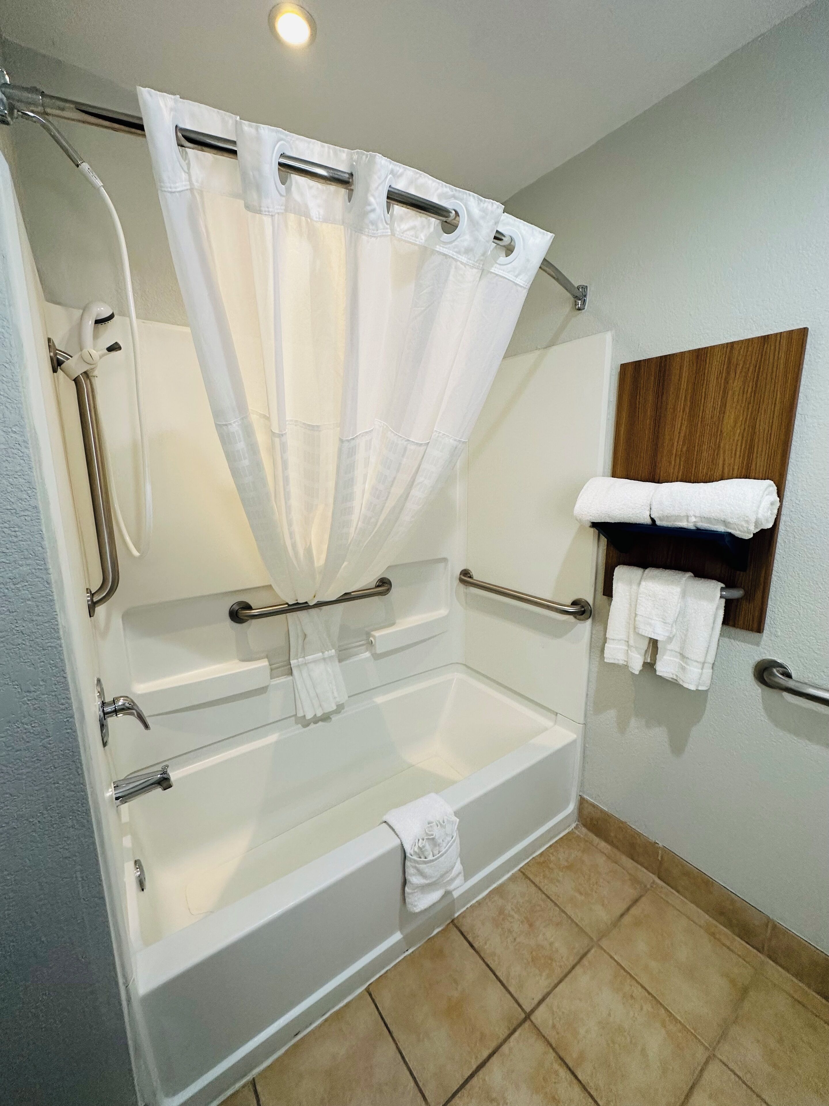 A standard bathroom with a bathtub, a shower curtain, a towel rack, and a handrail.