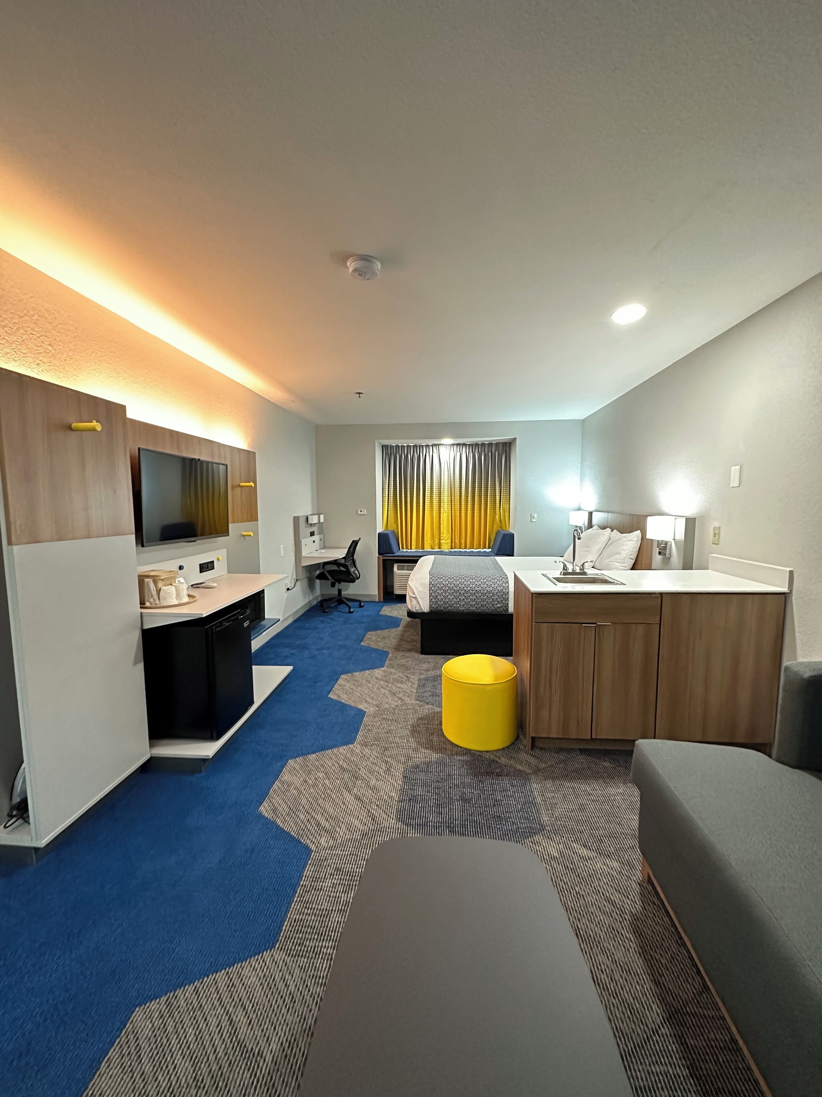 Una habitación de hotel compacta con kitchenette, una cama, un escritorio y un pequeño rincón de descanso.