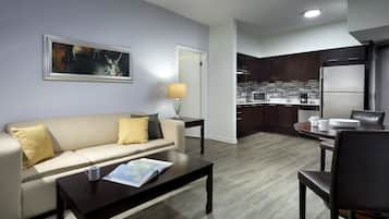 Een moderne woonkamer met een bank, salontafel en een eethoek. In de achtergrond is een keuken zichtbaar met een koelkast en magnetron.