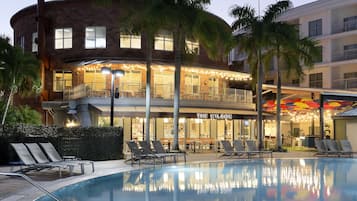 A hotel with a pool area, lounge chairs, and a restaurant.