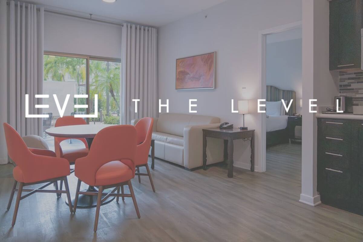 Quarto de hotel moderno com área de refeições, sofá, luminária e vista para o exterior.