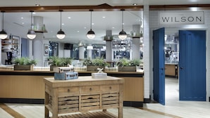 A modern hotel lobby with wooden furniture, pendant lighting, and a visible reception desk.