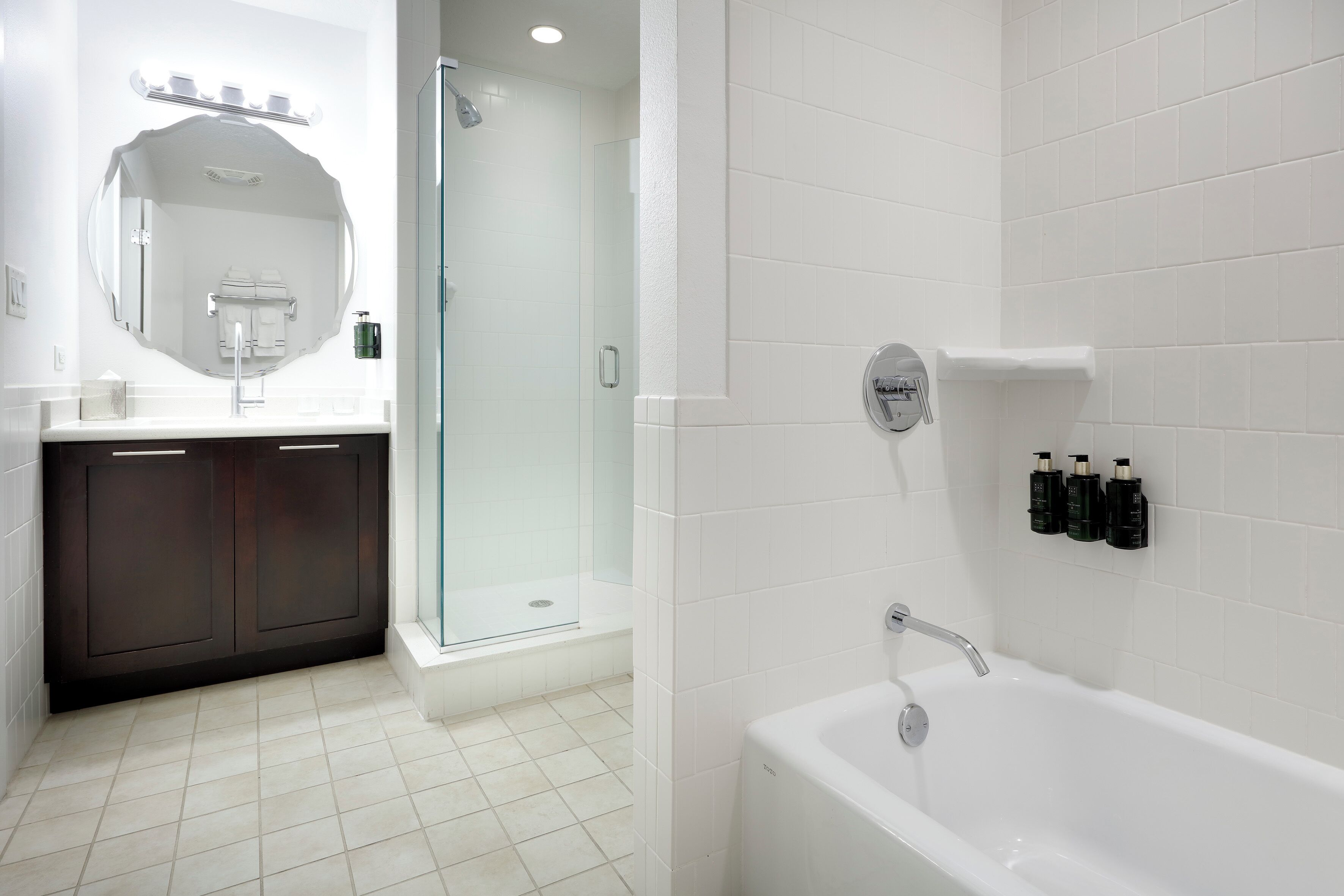 Un bagno moderno con una vasca da bagno bianca, una doccia vetrata e un mobile lavabo dai toni scuri.