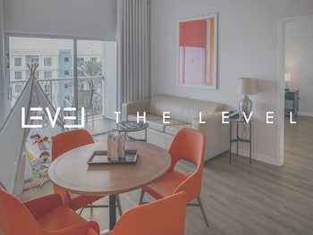 A modern hotel room with a balcony, a dining area with orange chairs, and a large window offering a view of greenery. at Melia Orlando Celebration