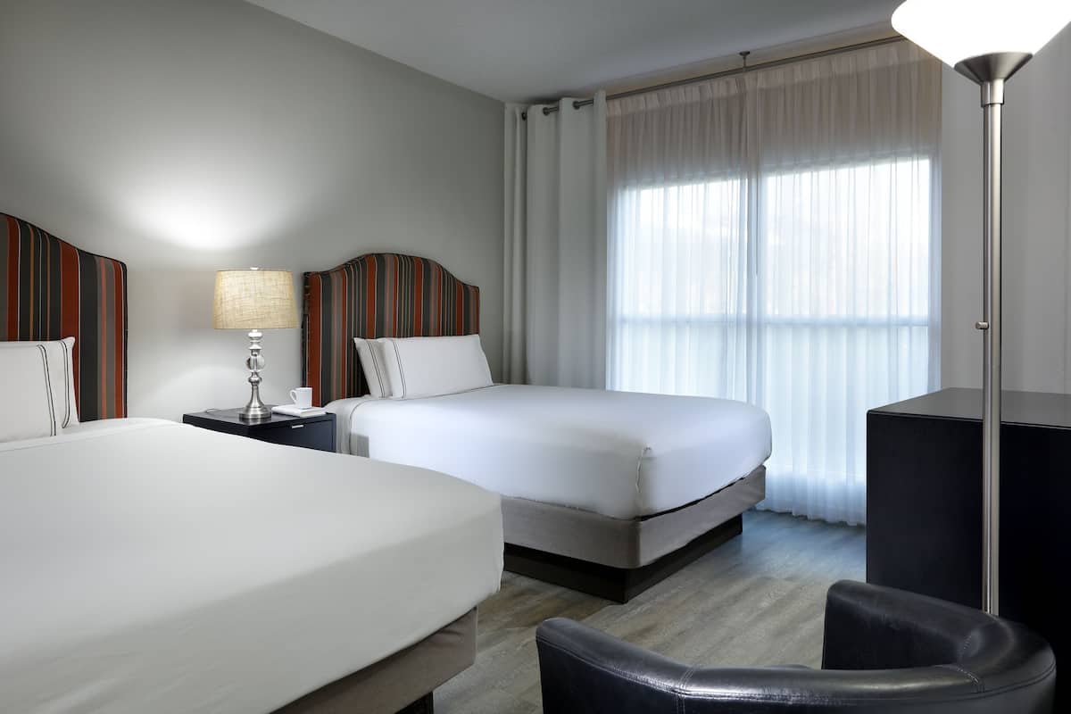 A hotel room with two beds, a desk, a lamp, and a chair.