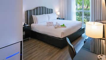 Una habitación de hotel con cama, mesita de noche, lámpara y vistas a zonas verdes por la ventana.