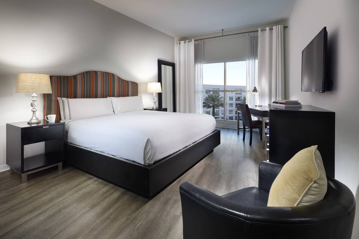 A modern hotel room with a large bed, a desk, a chair, and a TV.