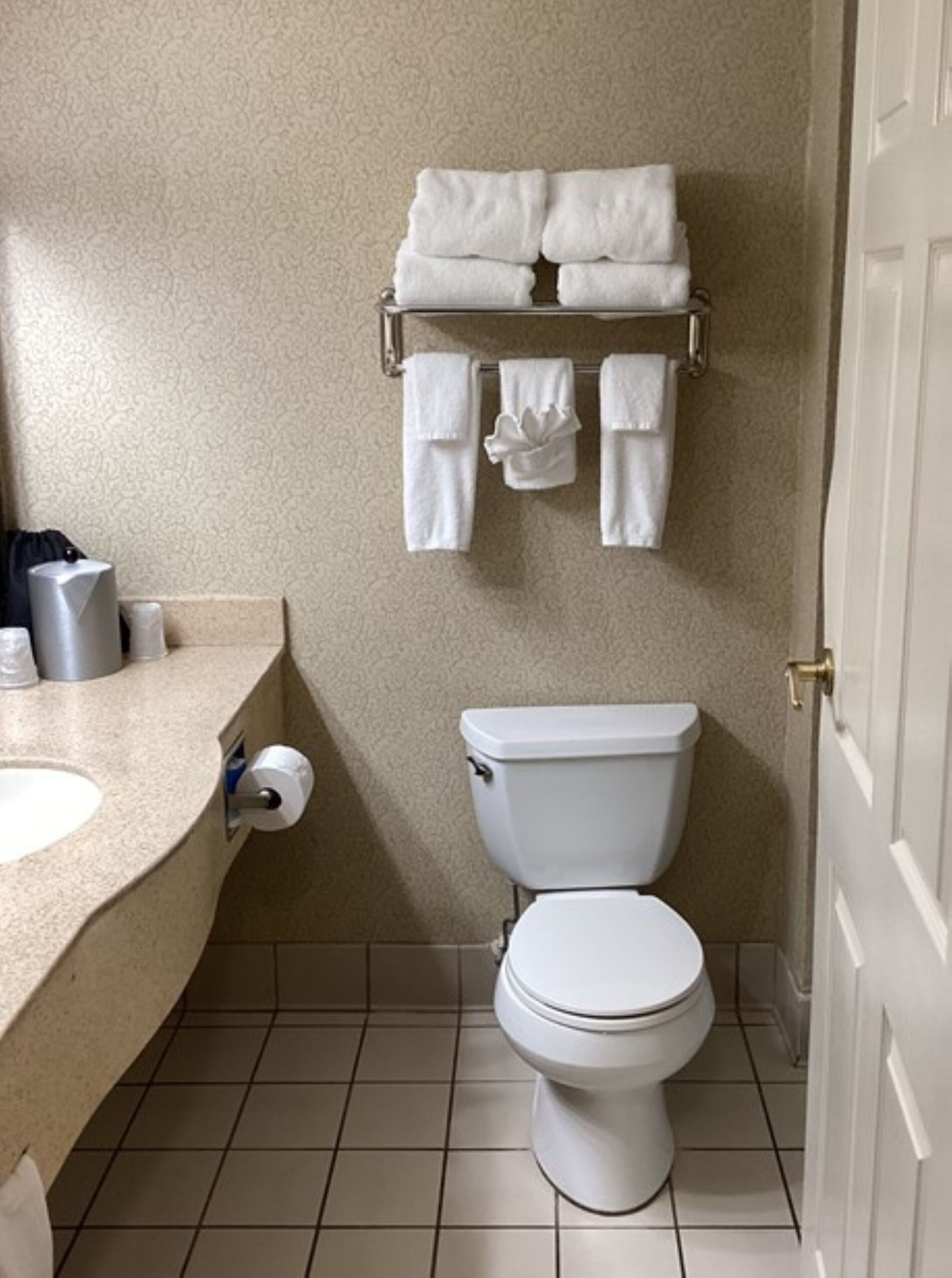 A small bathroom with a toilet, a sink, and a towel rack with folded towels.