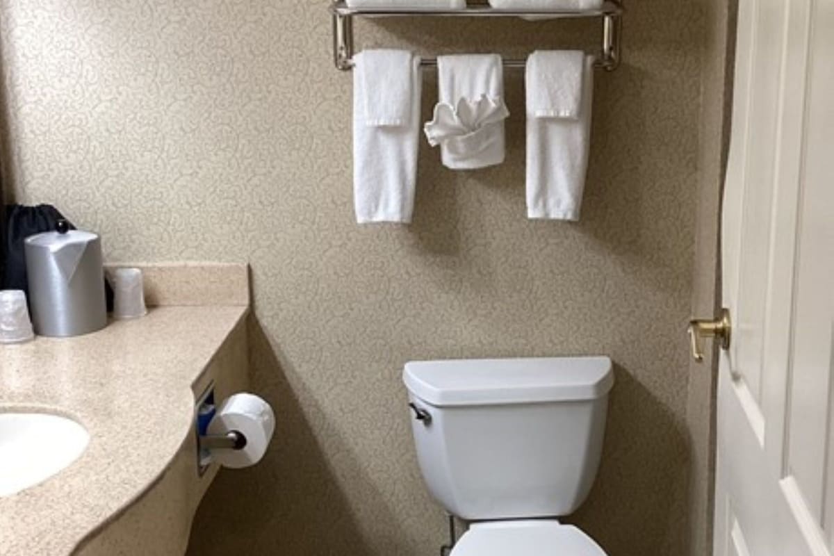 A small bathroom with a toilet, a sink, and a towel rack with folded towels.