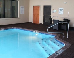 An indoor swimming pool with a 3 FT depth marking, a lifeguard on duty sign, and a wooden door in the background.